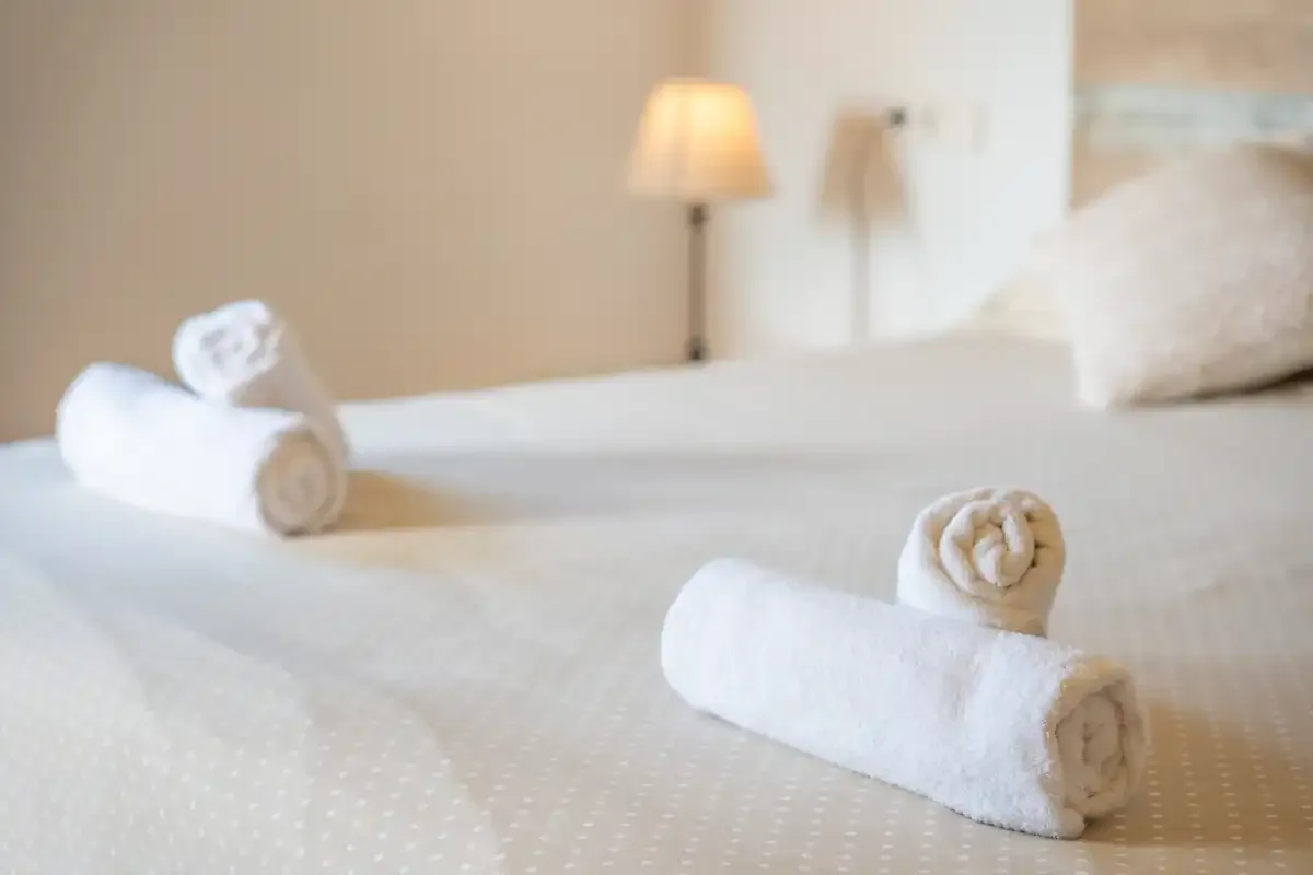 A bedroom with white bedding and rolled towels arranged on the bed.