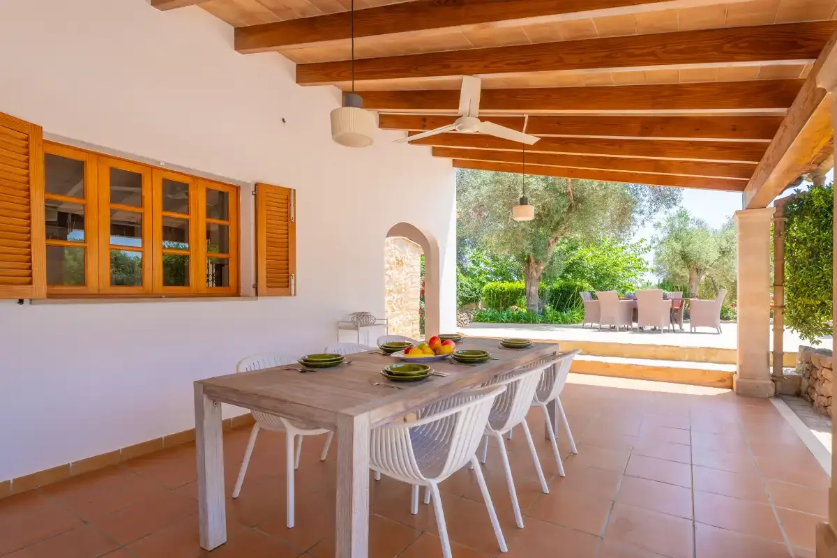 A covered outdoor dining area opens onto a patio with trees and seating.