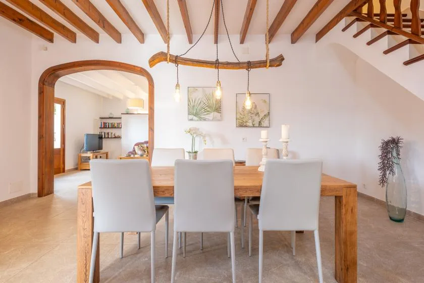 A dining area with a wooden table and light-colored seating beneath exposed ceiling beams.