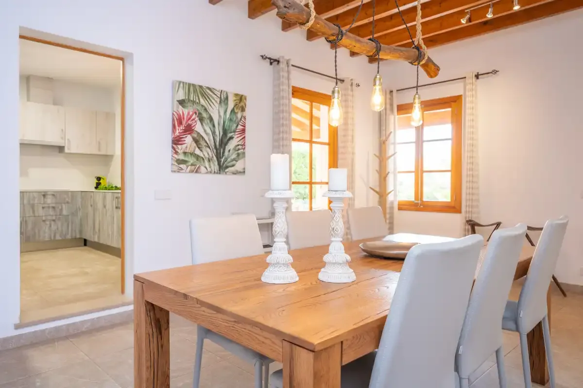 A dining area with a wooden table and chairs beside bright windows.
