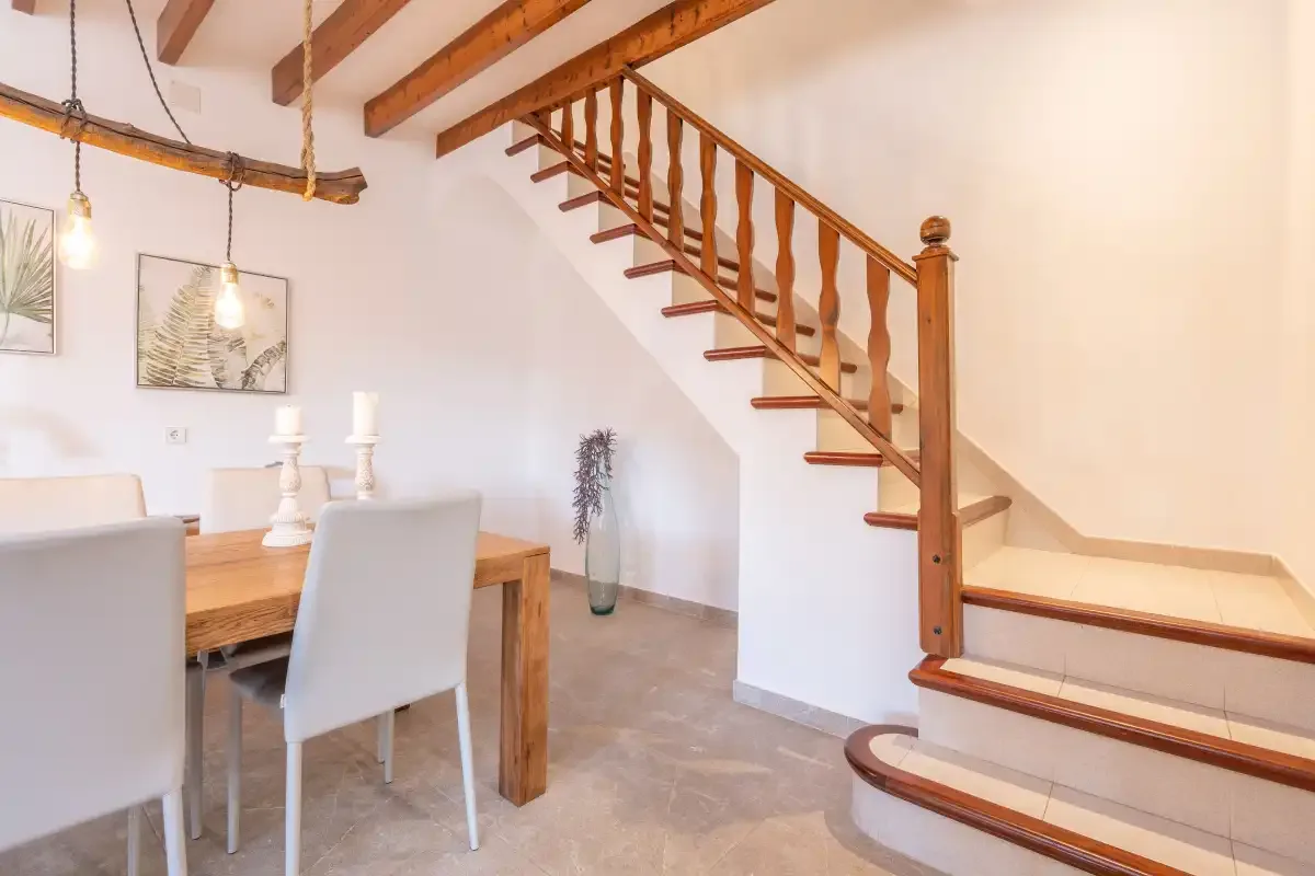 A dining area sits beneath a wooden staircase with exposed ceiling beams.