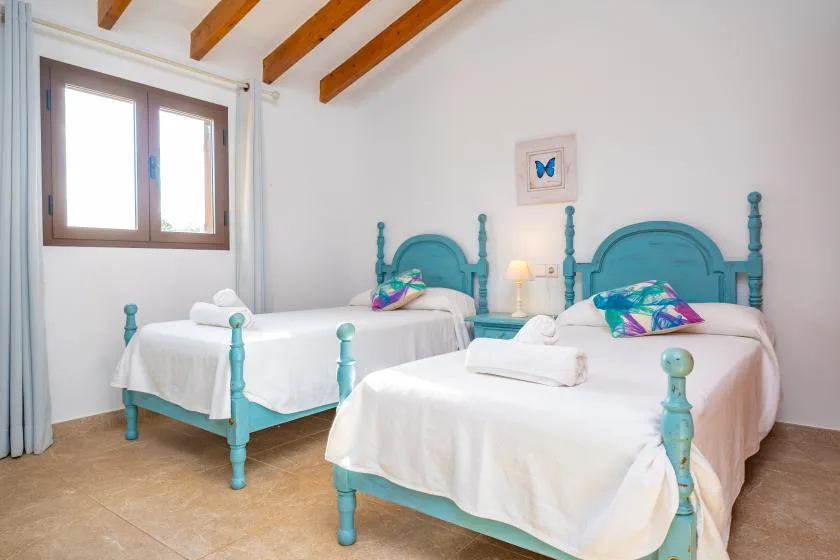 A bright bedroom with two beds, turquoise frames, and exposed wooden ceiling beams.