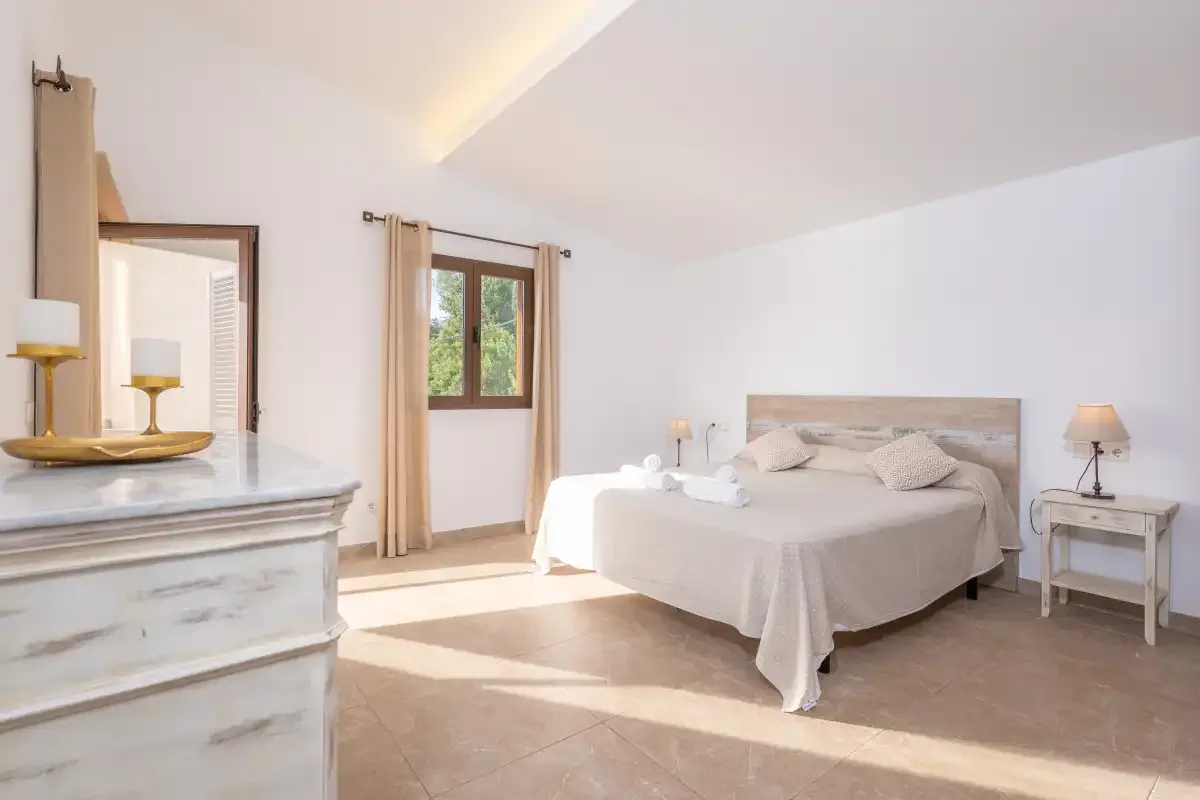 A bright bedroom with a bed beside a window and bedside tables.
