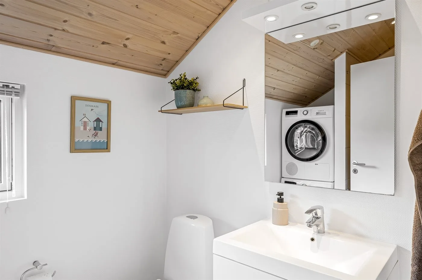 A bathroom with a sink and a washing machine reflected in the mirror.