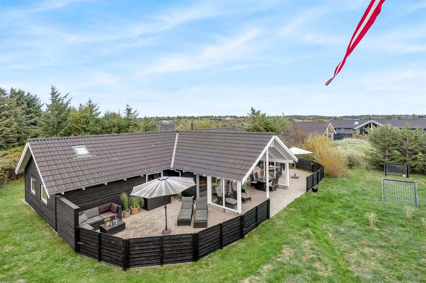 A dark-sided house has a broad outdoor deck with seating and an umbrella.