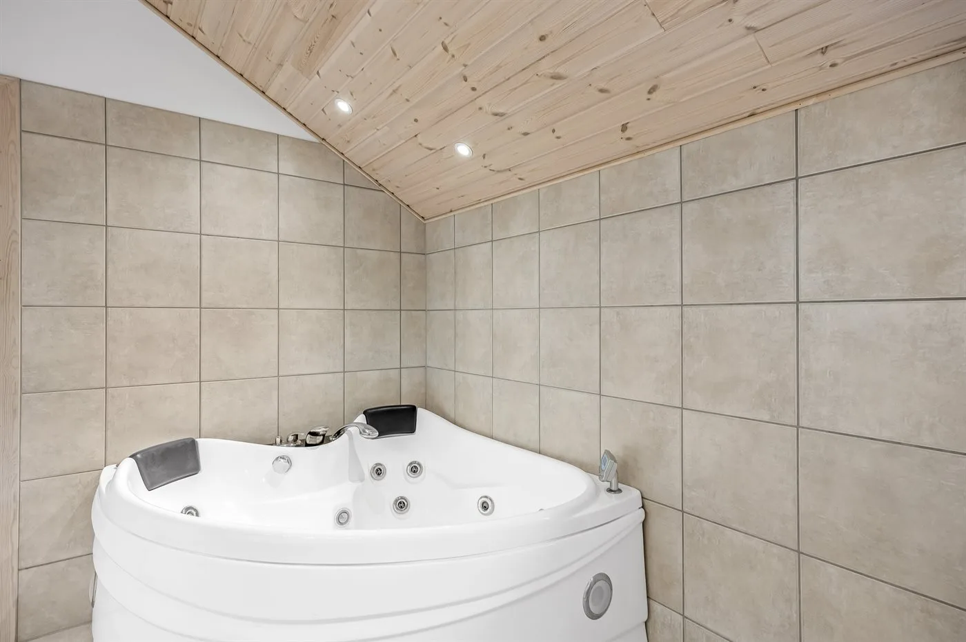 A corner whirlpool tub sits beneath a sloped wooden ceiling in a tiled bathroom.