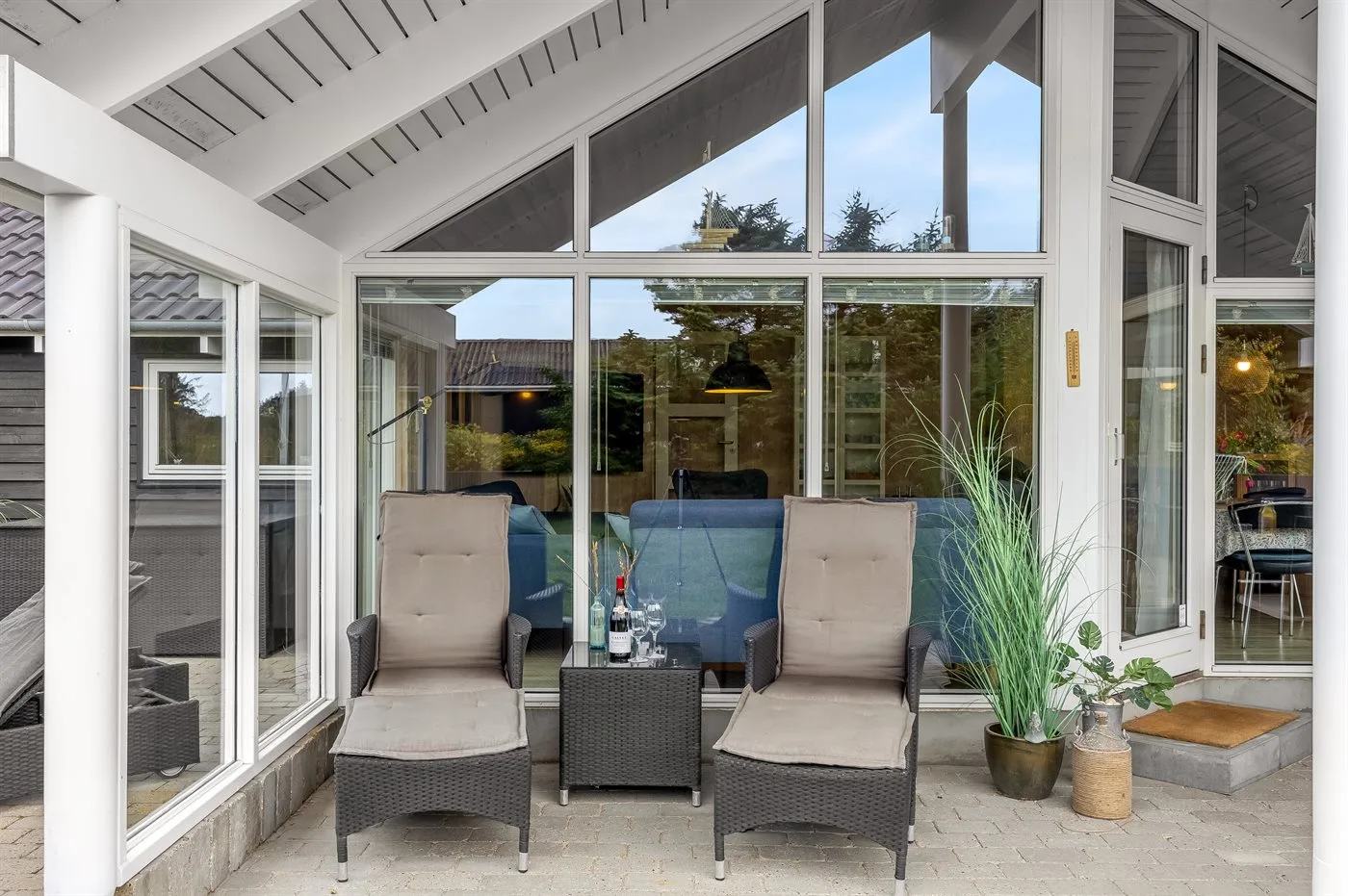 A covered patio with cushioned seating and a small table faces glass windows.