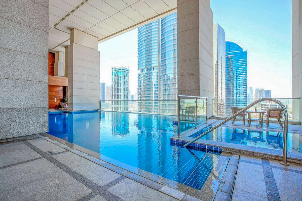 Una piscina cubierta con una barandilla metálica y edificios de la ciudad visibles más allá de las ventanas.