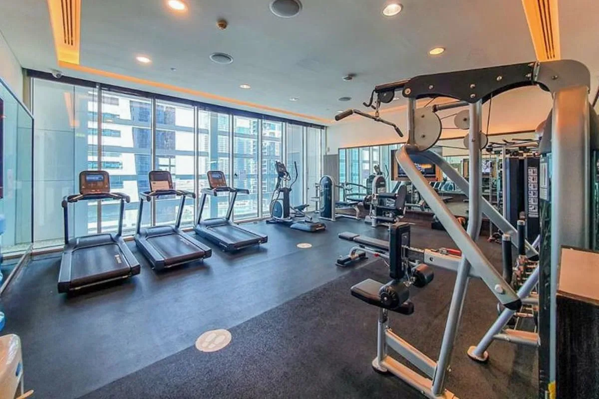Un gimnasio con equipo de ejercicio y grandes ventanales.