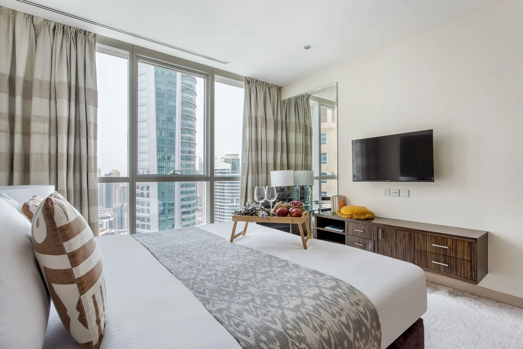 Un dormitorio luminoso con una ventana grande, cortinas estampadas y un televisor.
