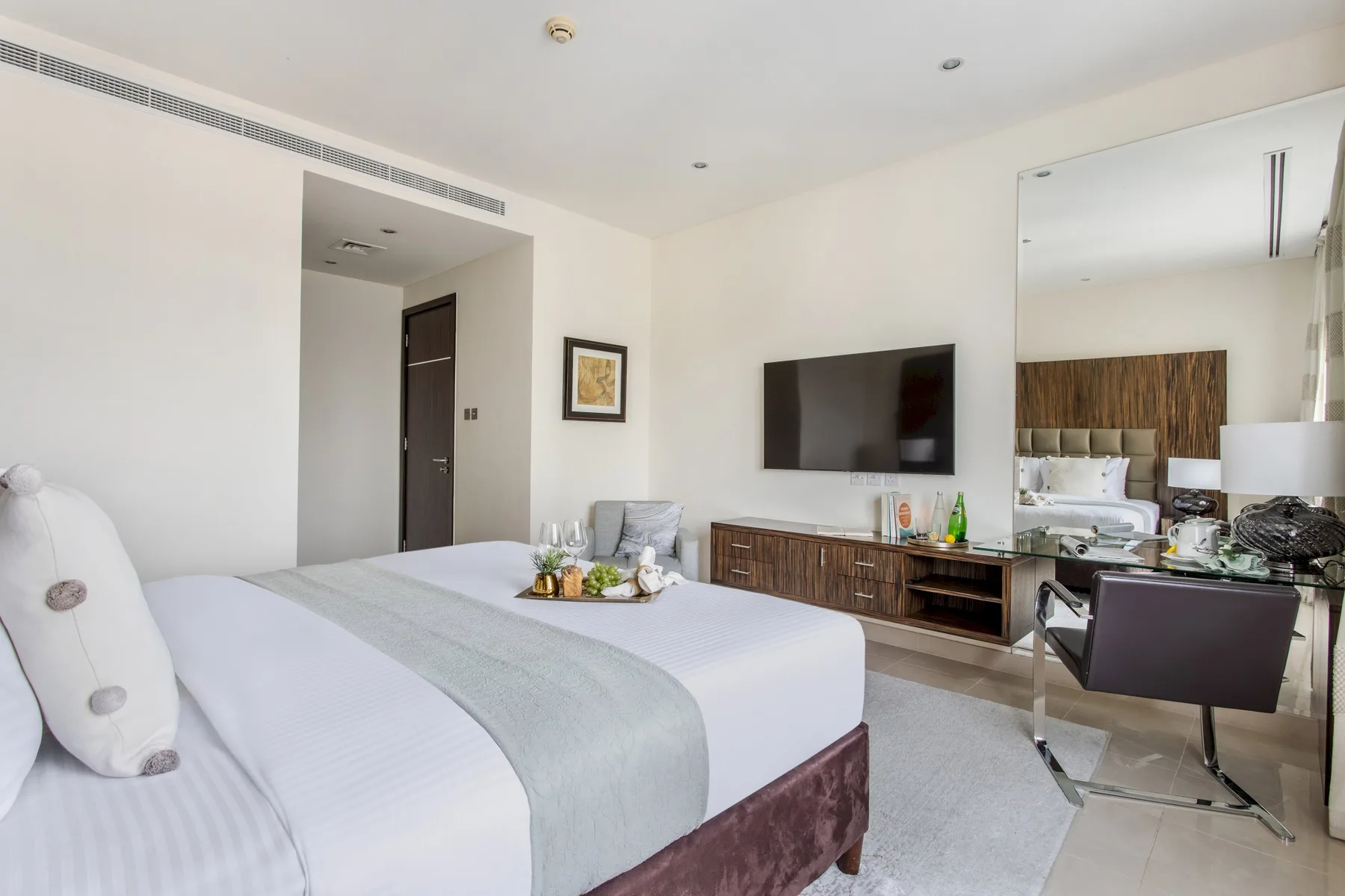 Un dormitorio luminoso con una cama bien tendida y un televisor montado en la pared.