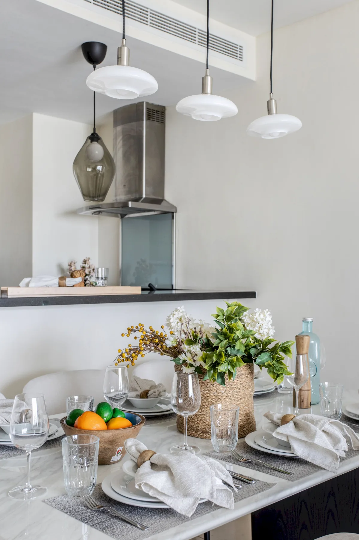 Una mesa de comedor está puesta con cristalería, platos y un arreglo de flores.