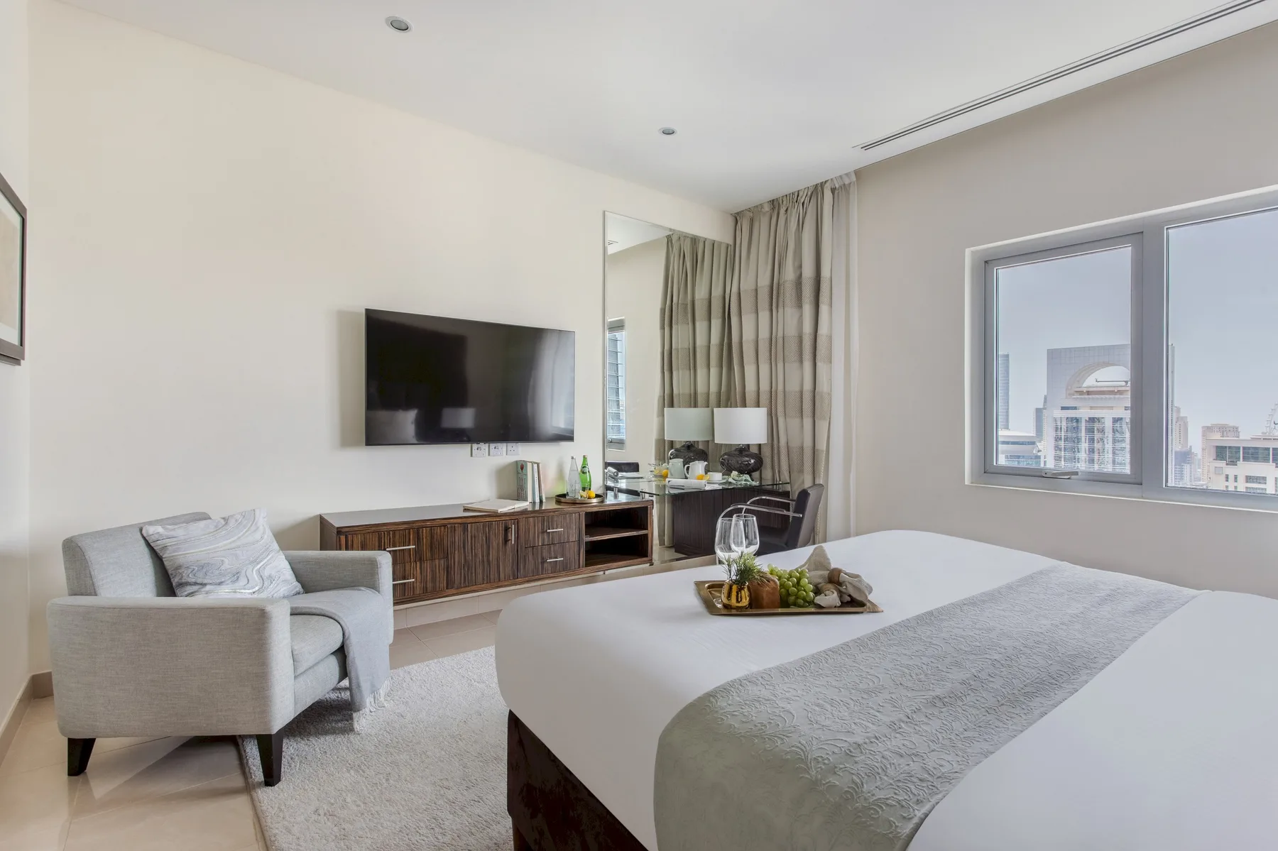 Un dormitorio con una cama grande, un televisor y una ventana con vistas a edificios cercanos.