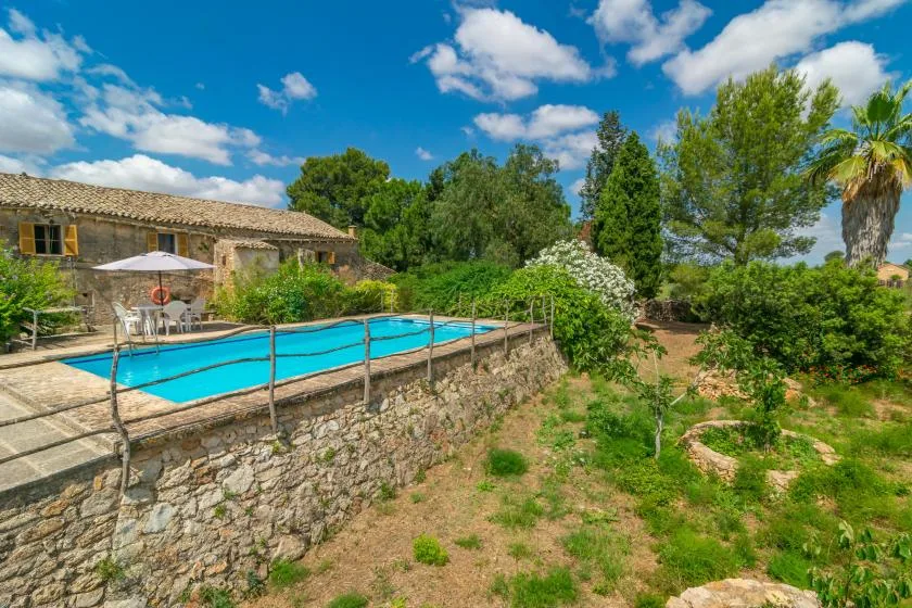 A swimming pool beside a stone house, surrounded by greenery.