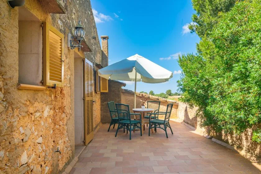 A sunny stone terrace has outdoor seating beneath a large umbrella.