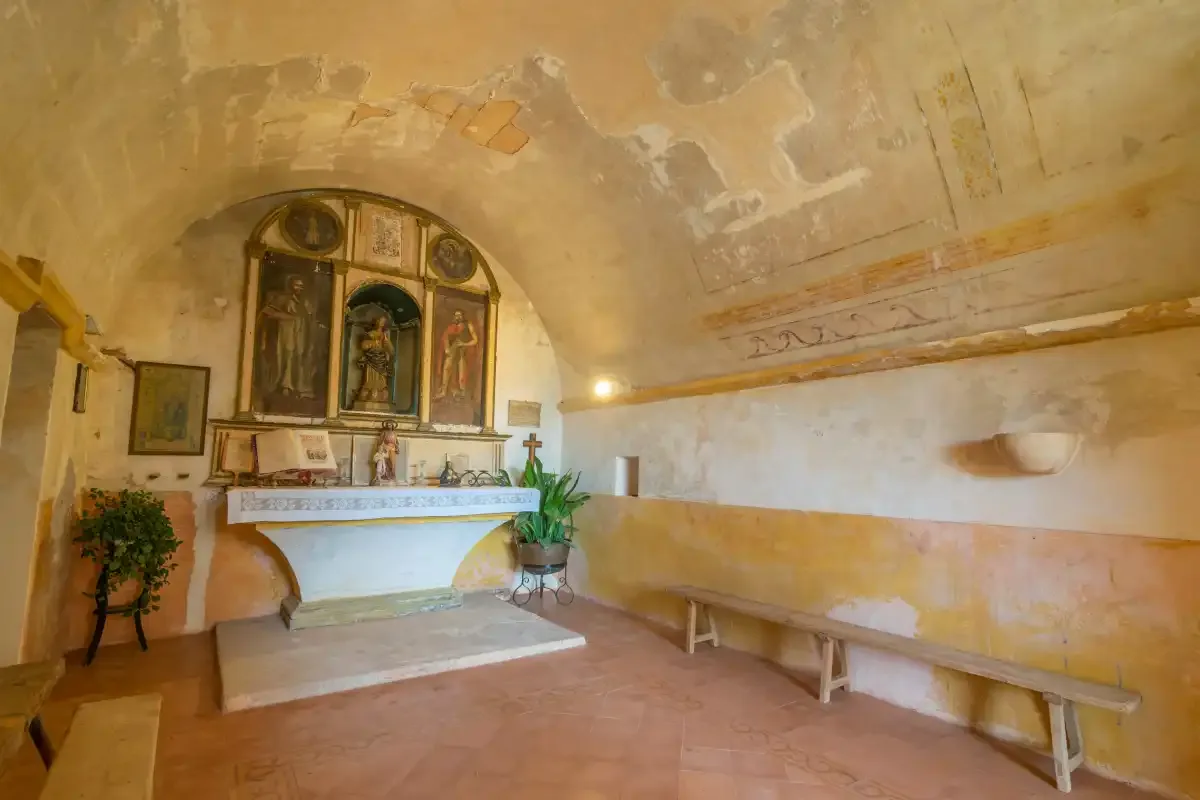 A chapel interior with a small altar and long built-in seating.