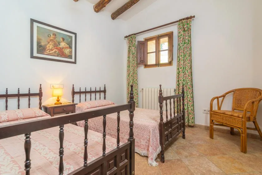 A bedroom with two beds, a wooden chair, and a window with floral curtains.