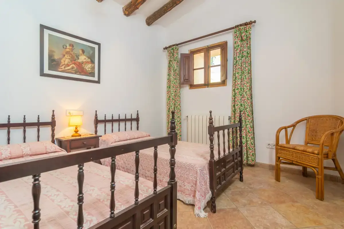 A bedroom with two beds, a window, and a wicker chair.