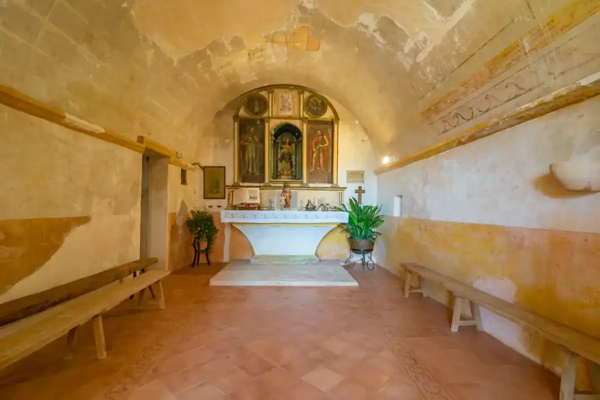 A small chapel with an altar, wall paintings, and wooden benches.