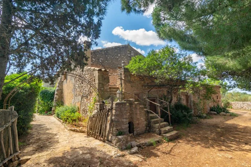 A weathered stone building stands among trees beside a dirt path.
