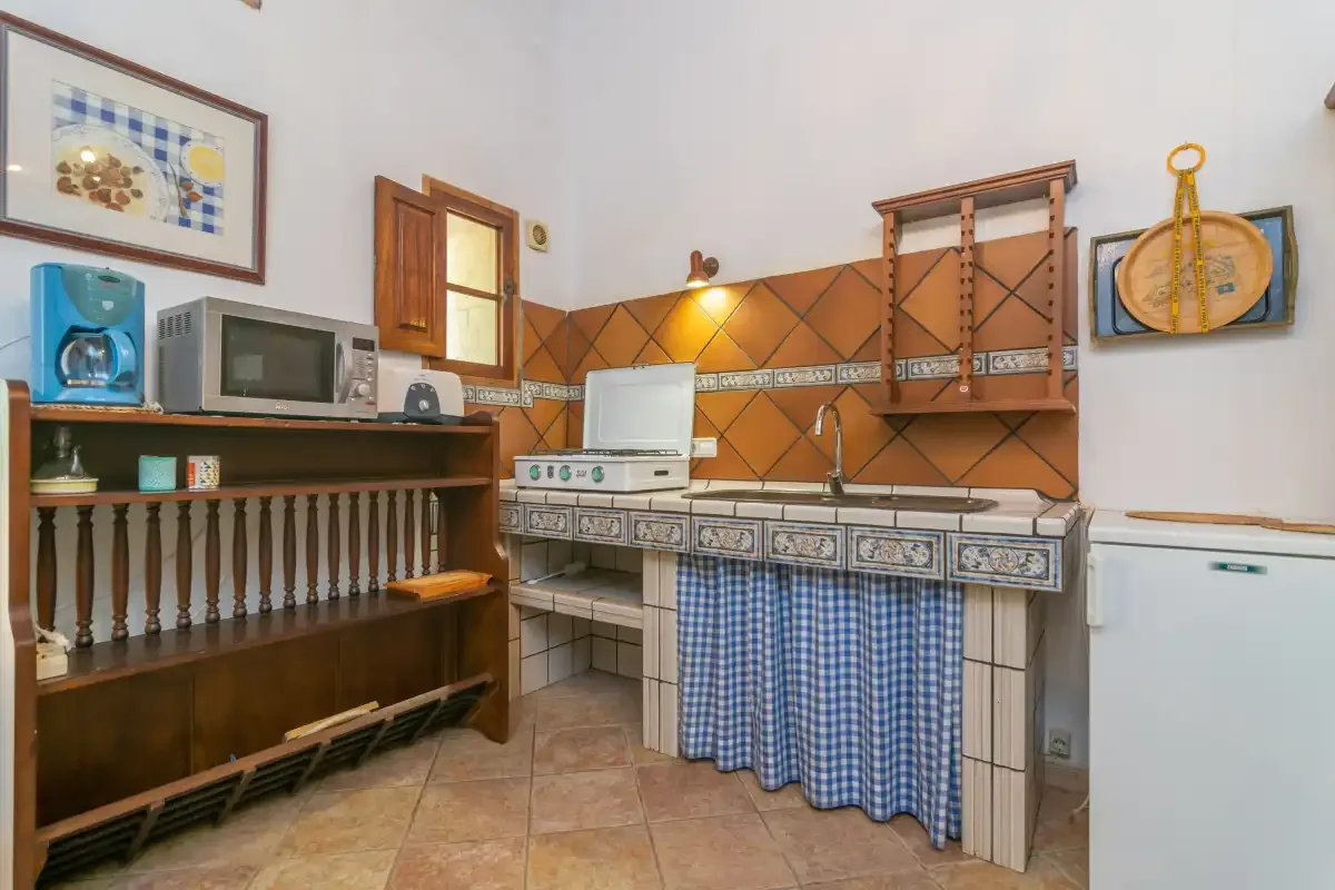 A rustic kitchen with a tiled counter, sink, and blue checked curtains.