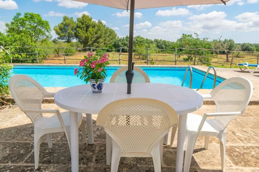 A patio table and seating sit beside a swimming pool under a large umbrella.