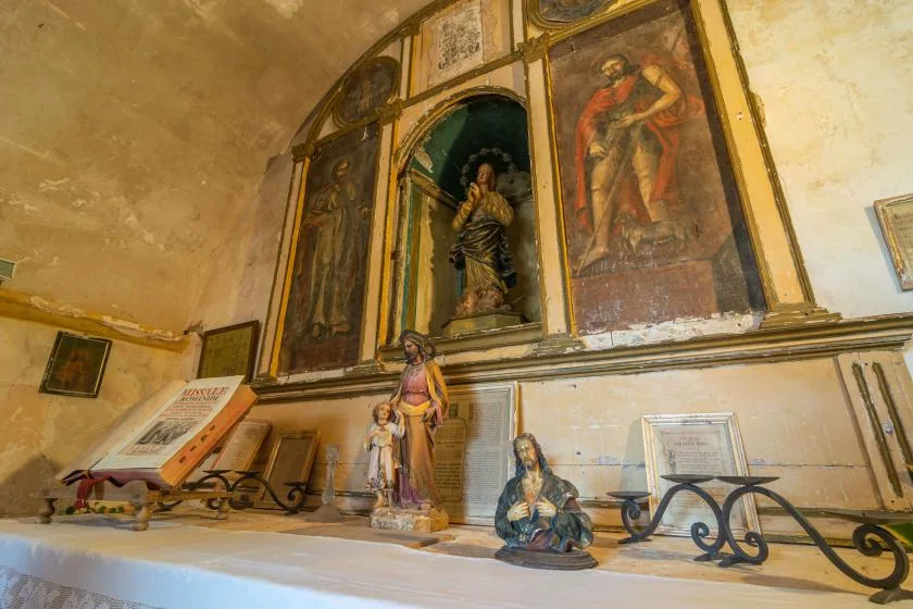 A small chapel interior with religious paintings and statues along the walls.