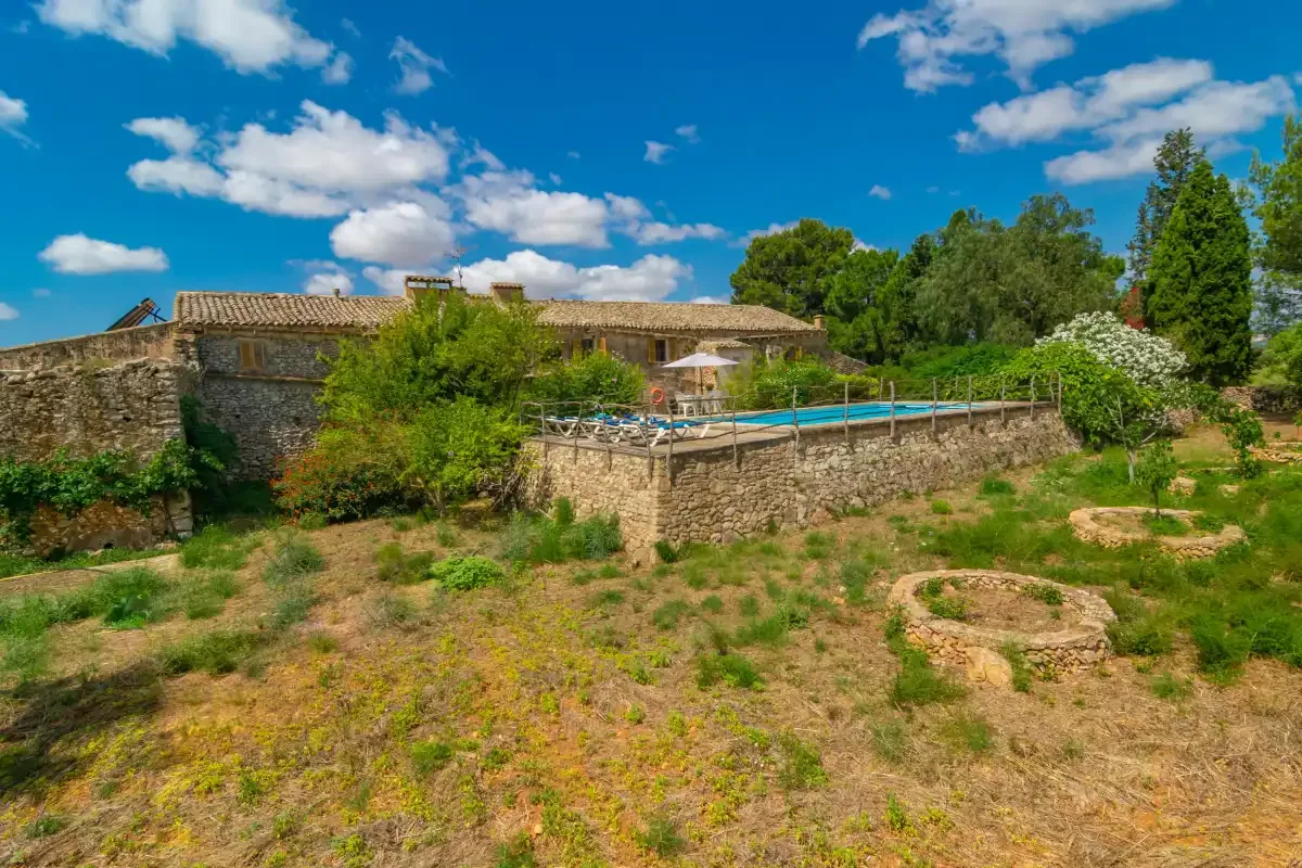 A stone building and swimming pool sit amid a dry, grassy landscape.