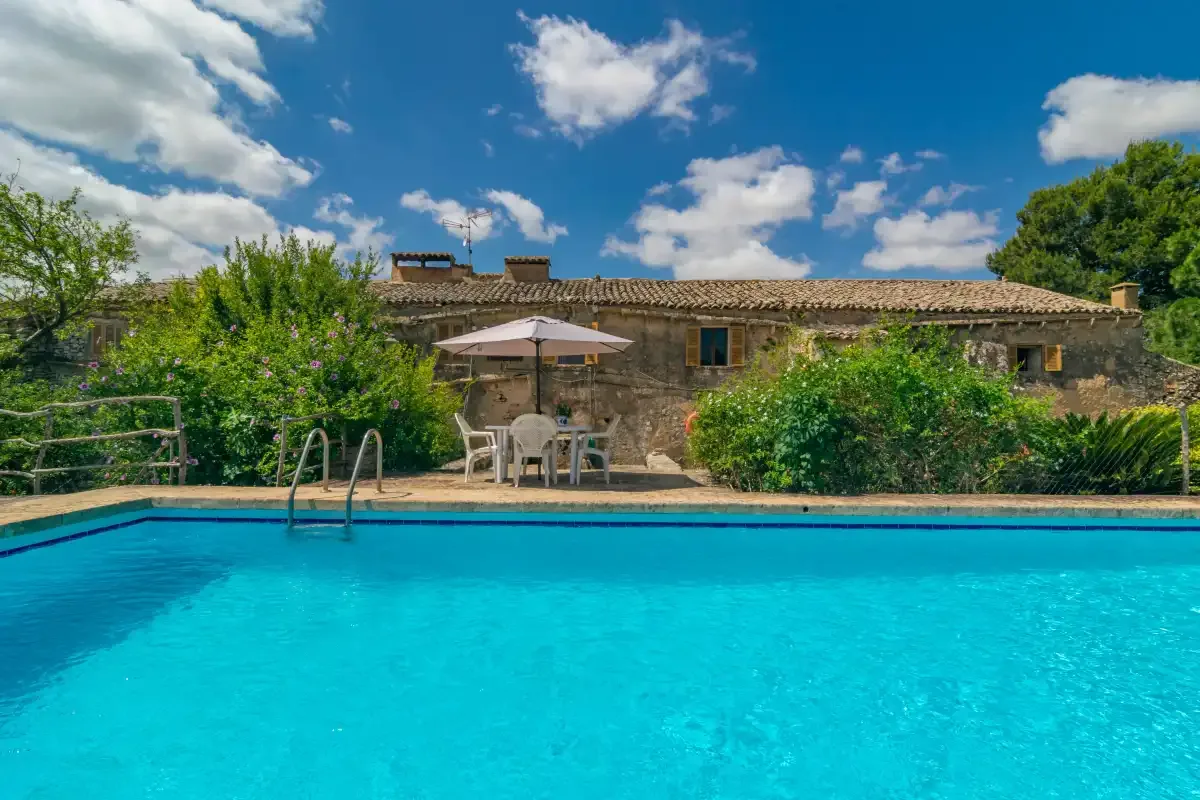 A swimming pool sits in front of a stone house and outdoor seating.