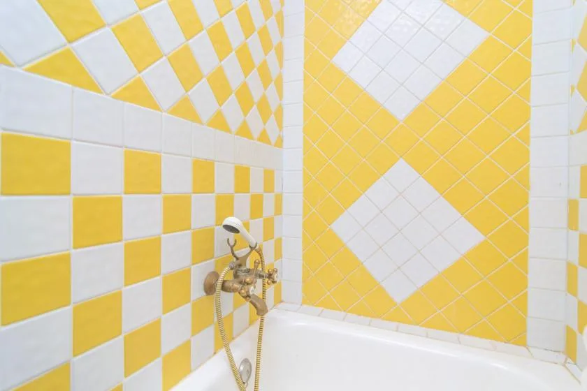 A bathtub sits against yellow-and-white tiled bathroom walls, with a wall-mounted faucet.