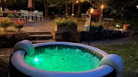 An outdoor inflatable hot tub glows beside a garden patio at night.