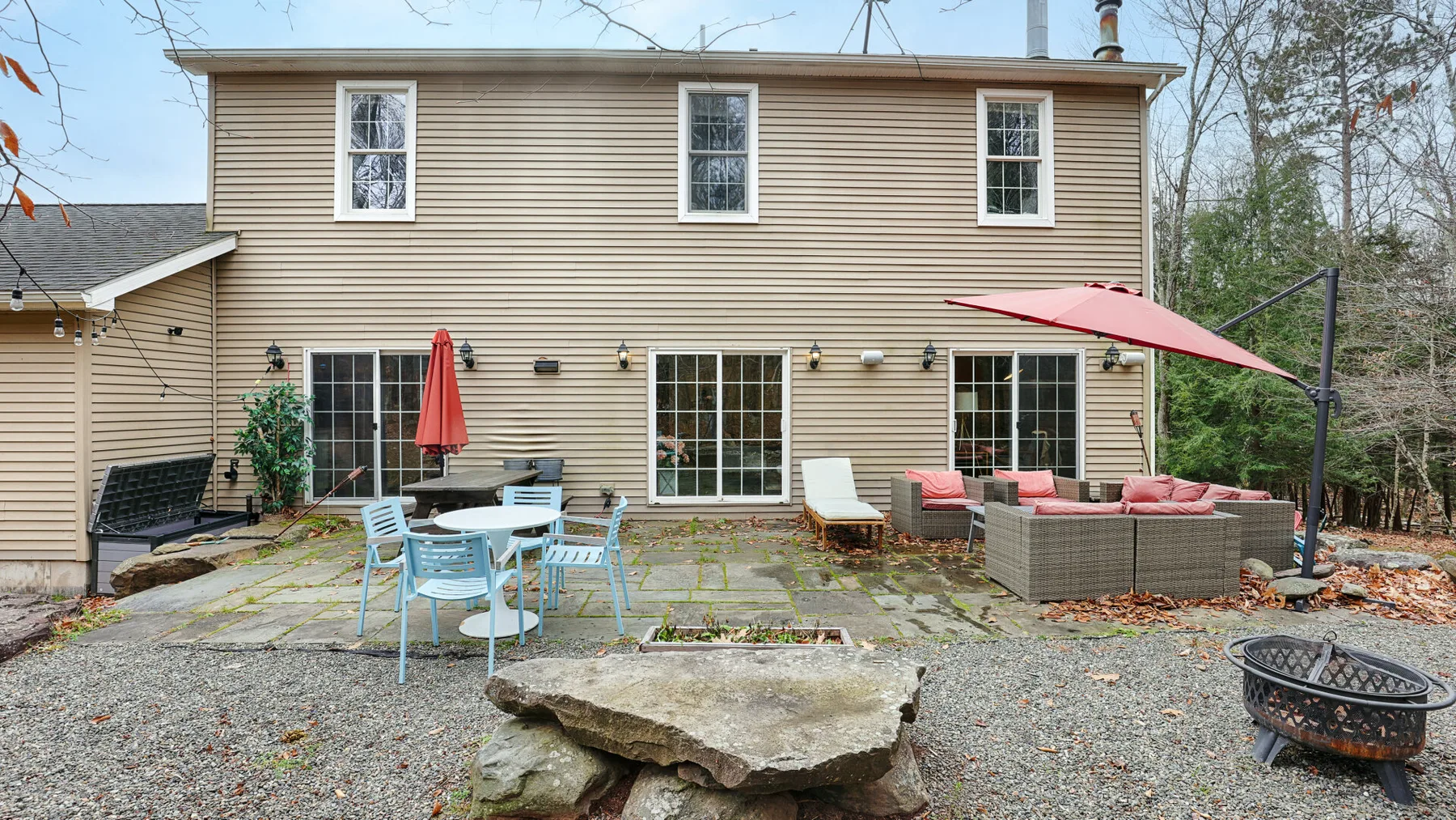A two-story house faces a patio with outdoor seating and a red umbrella.