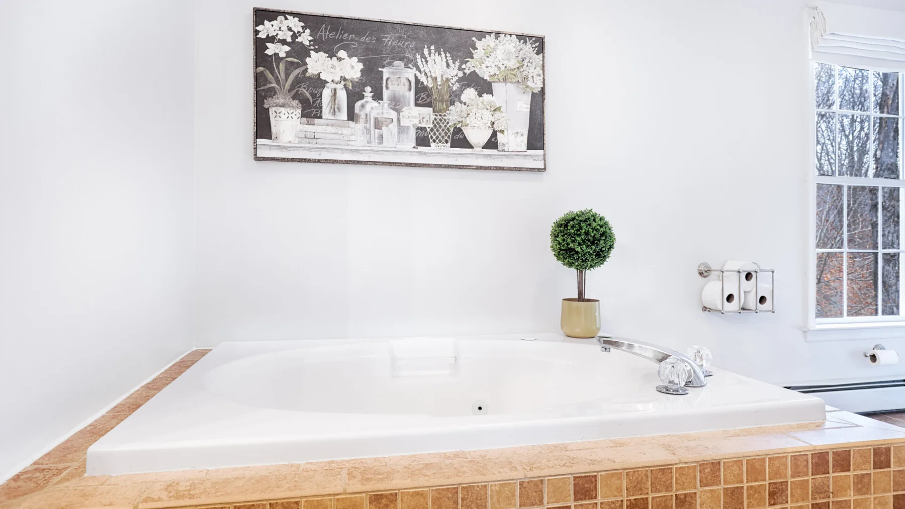 A bathroom with a large bathtub beneath framed floral artwork.