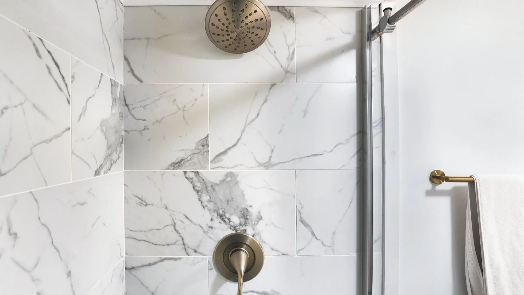 A marble-tiled shower with a round overhead showerhead and wall-mounted controls.