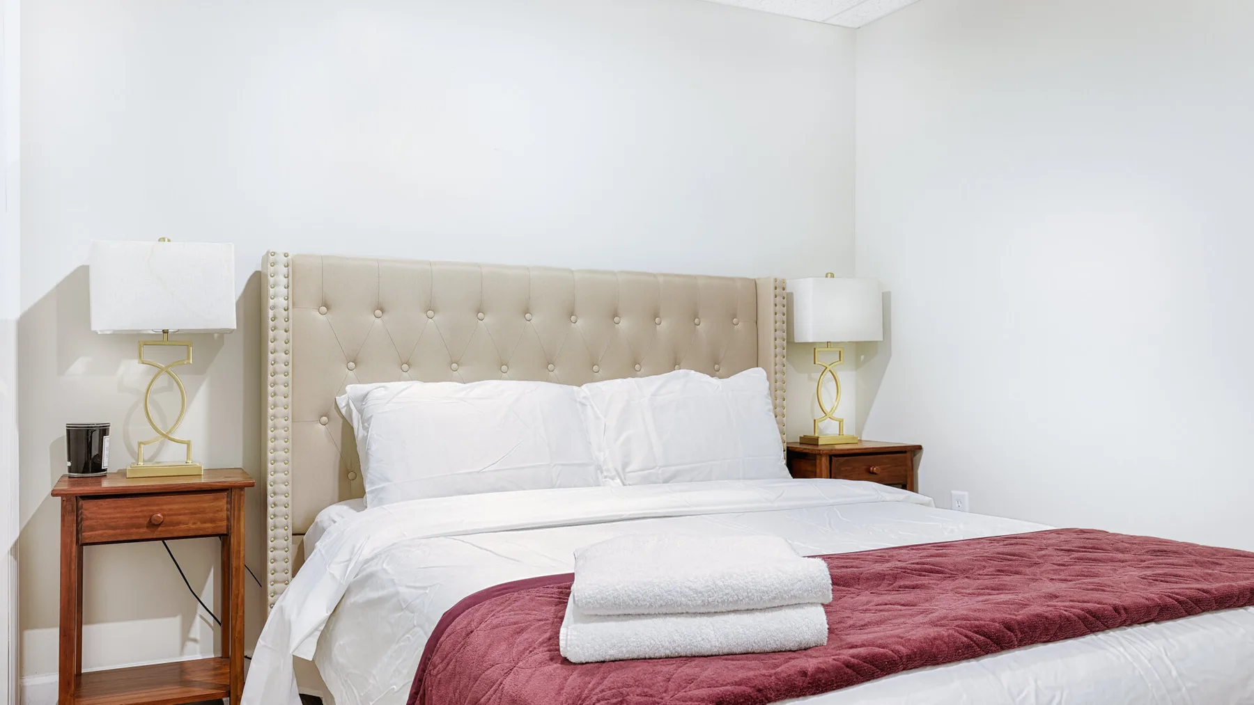 A bedroom with a tufted headboard, white bedding, and a burgundy blanket.