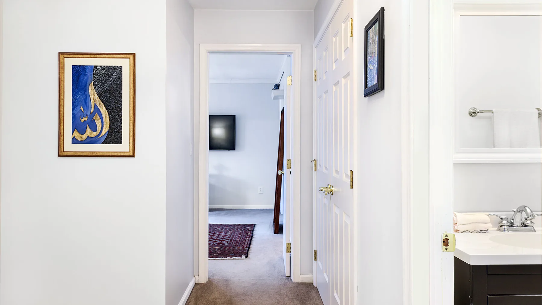 A bright hallway opens onto a room with a wall-mounted television and rug.
