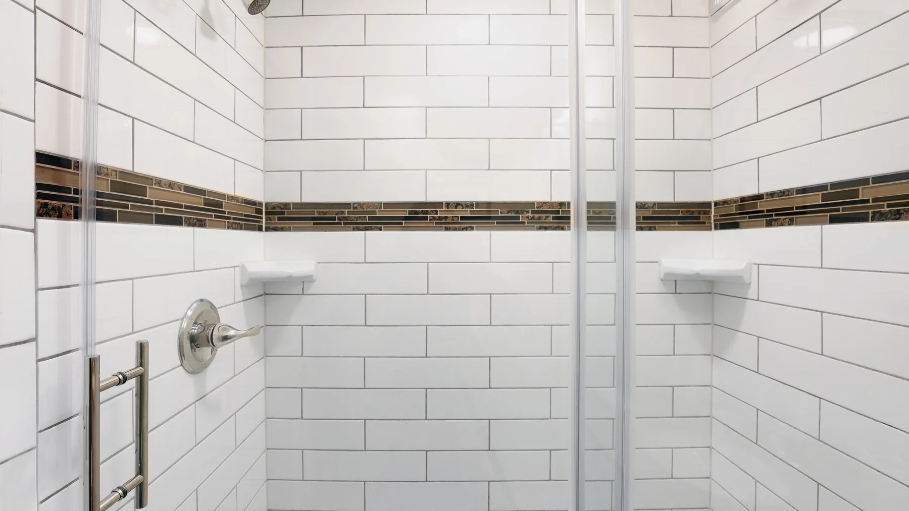 A tiled shower with white walls and a dark decorative horizontal band.