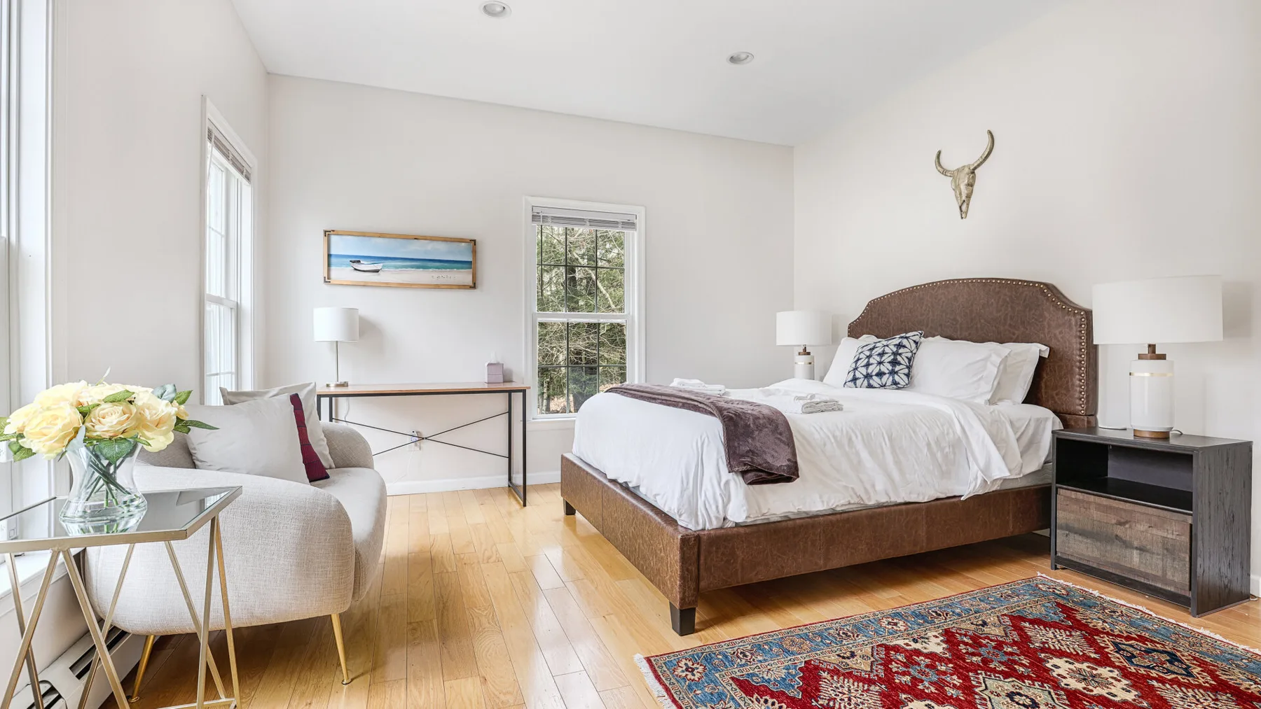 A bright bedroom with a bed, seating, and a colorful rug.