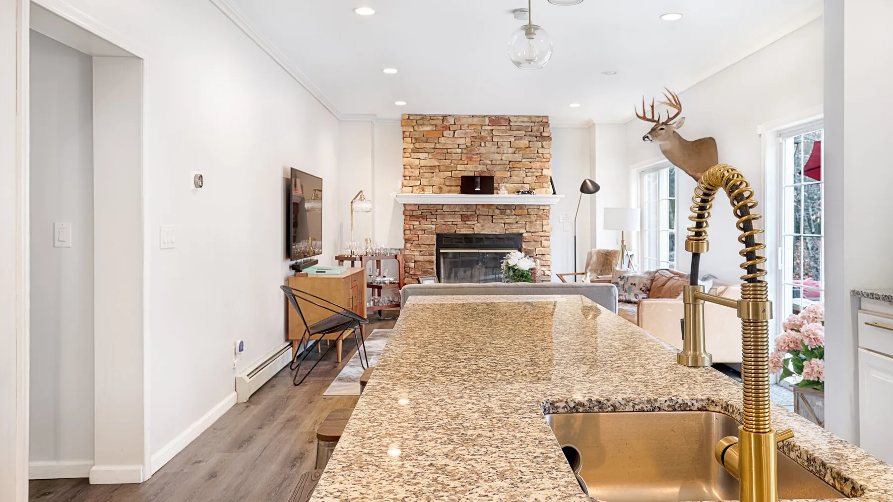 A bright open-plan living room and kitchen with a stone island and fireplace.
