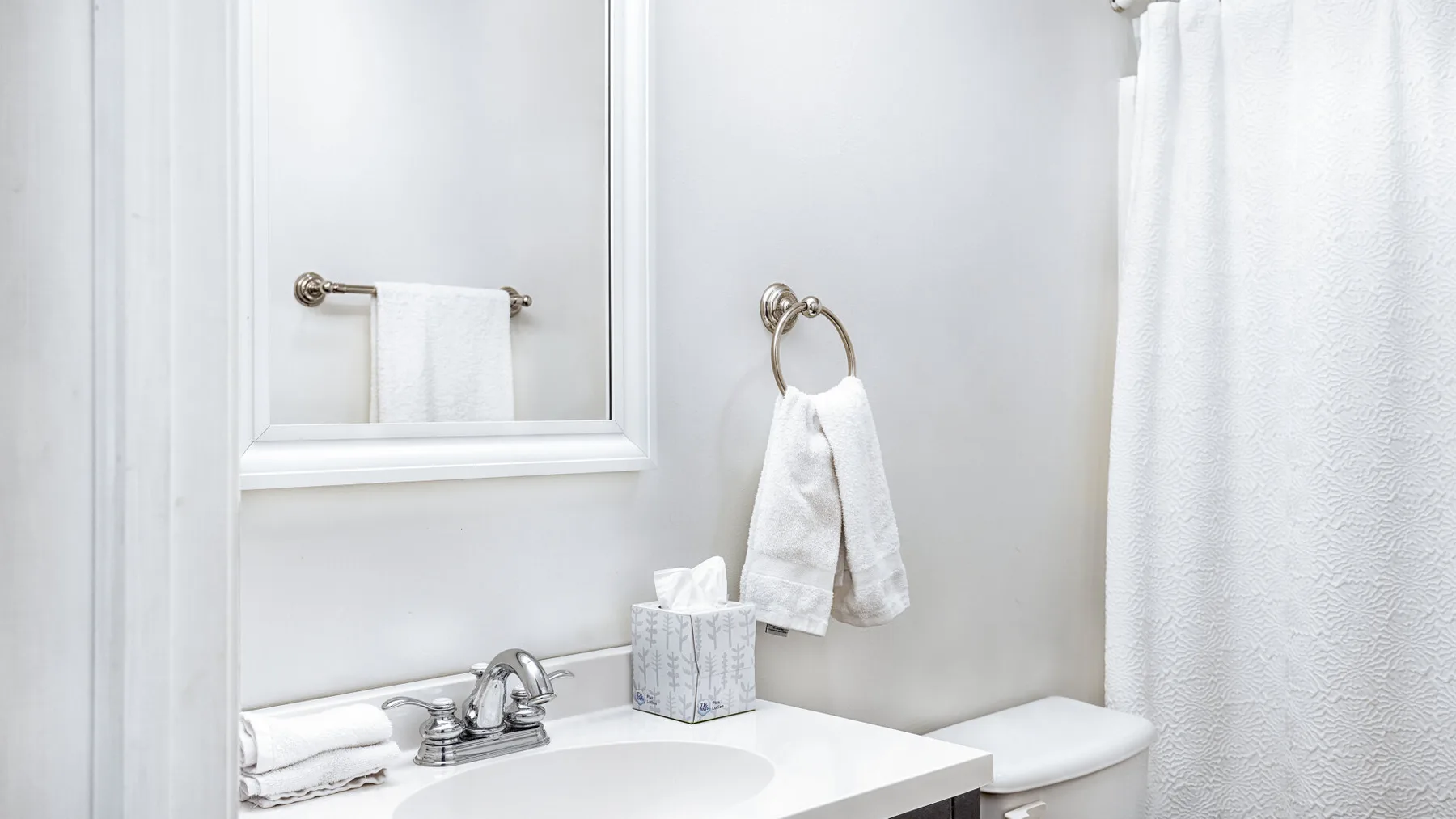 A bright bathroom with a sink, mirror, and white shower curtain.