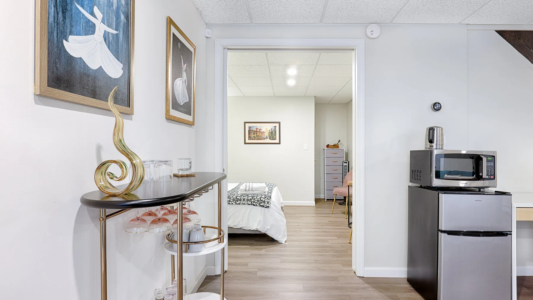 A bedroom is visible through the doorway beside a small kitchenette.