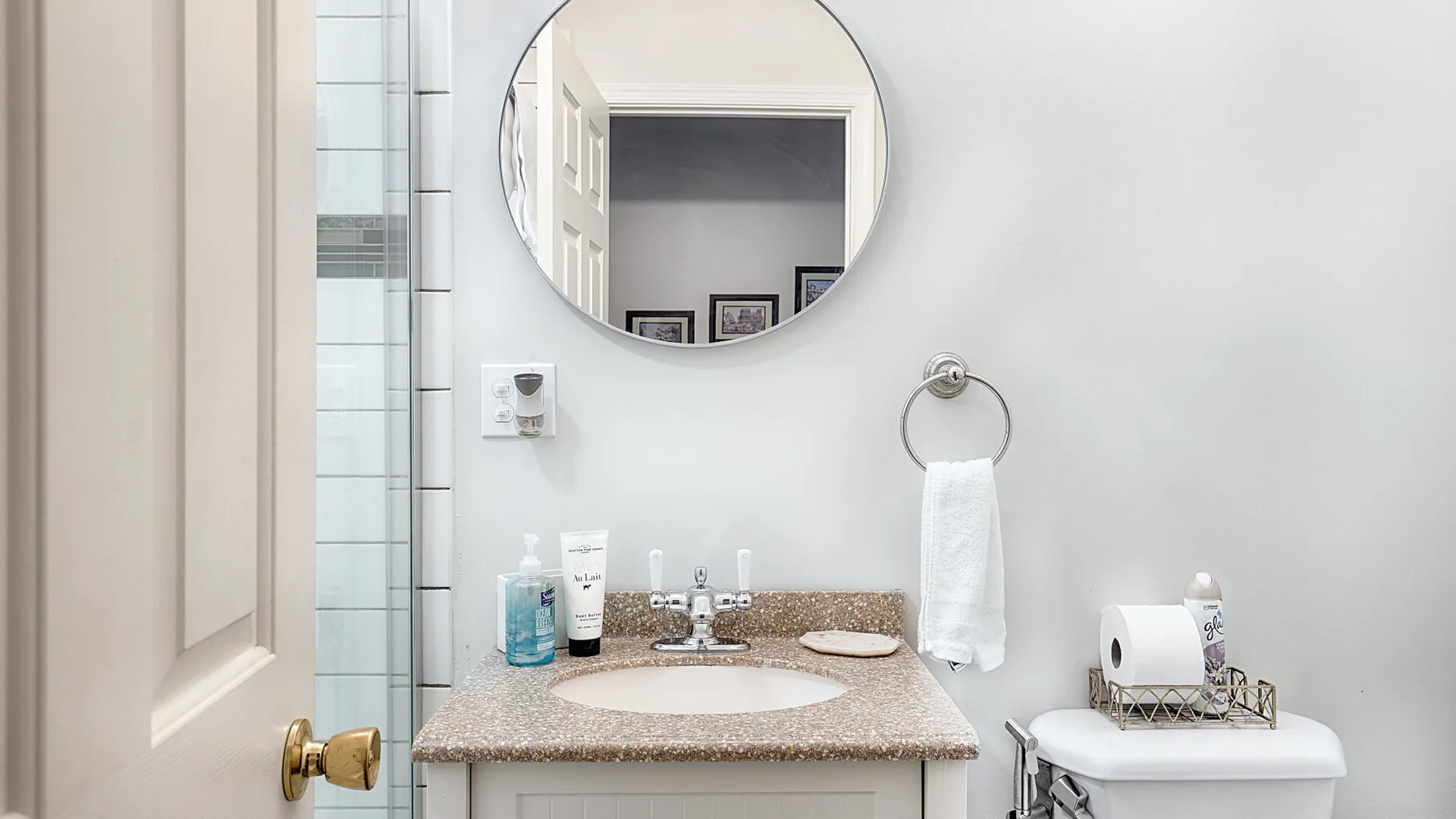 A bright bathroom with a vanity, round mirror, and toilet.