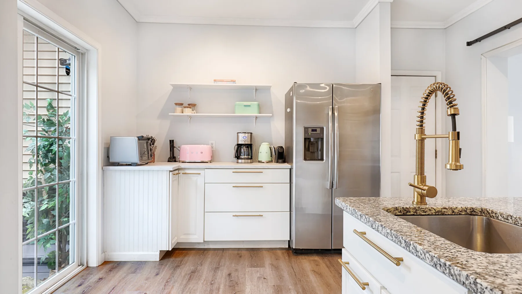 A bright kitchen with white cabinetry, stainless steel appliances, and a stone countertop.