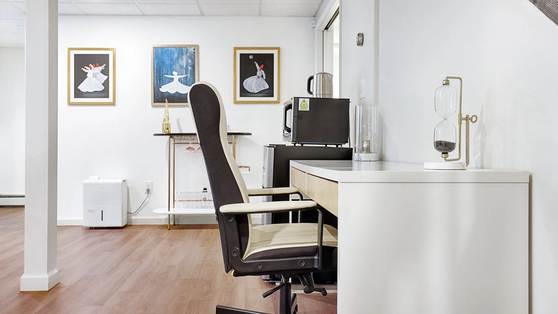A bright office workspace with a desk, chair, and framed artwork on the wall.
