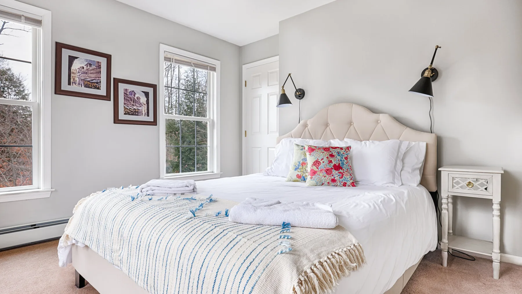 A bright bedroom with a white bed, colorful cushions, and framed artwork.