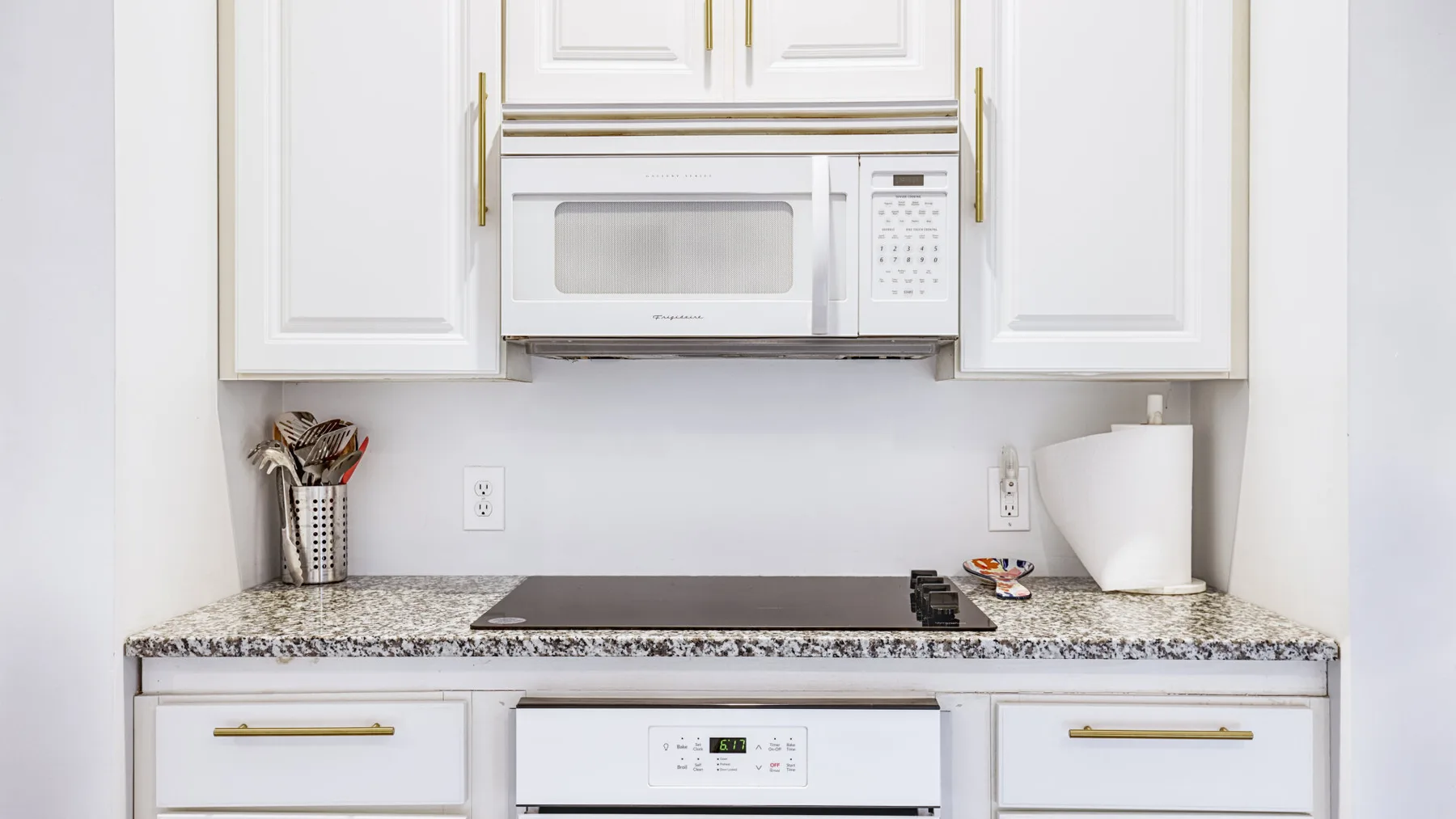 A compact kitchen with white cabinets, a microwave, and a cooktop.