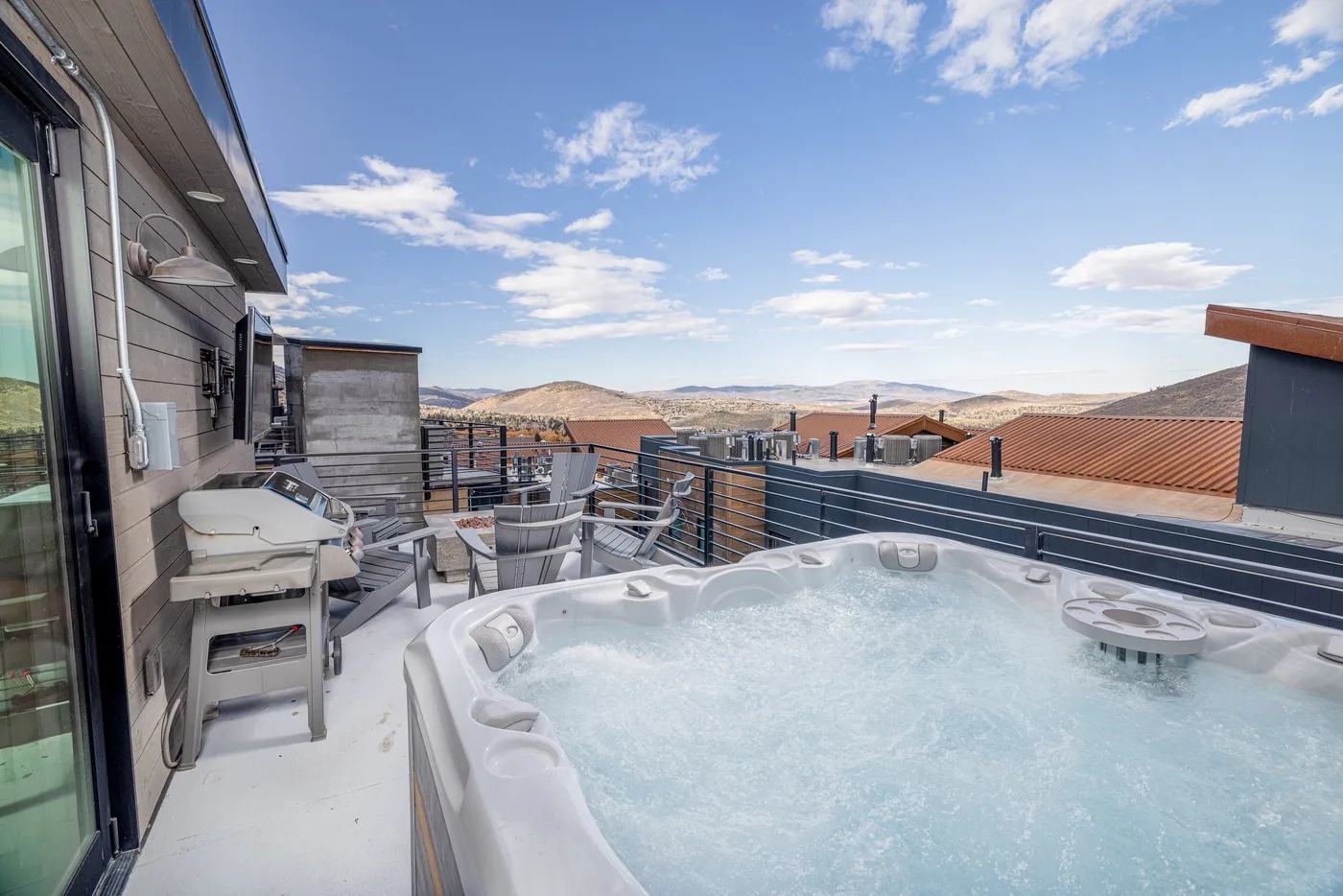 A rooftop terrace features a bubbling hot tub, outdoor seating, and distant hills.