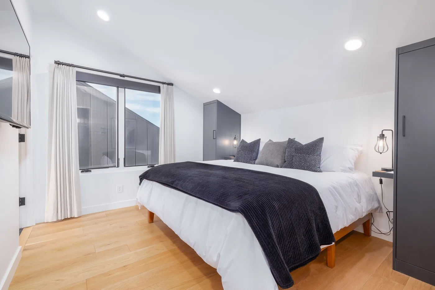 A bedroom with a bed, dark bedding, and a large curtained window.