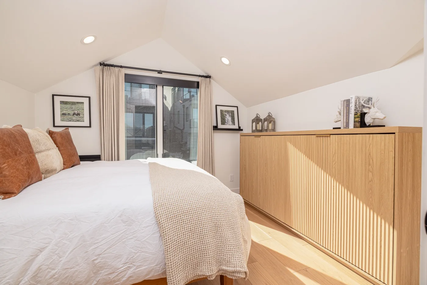 A bright bedroom with a bed beside a large window and a wooden cabinet.