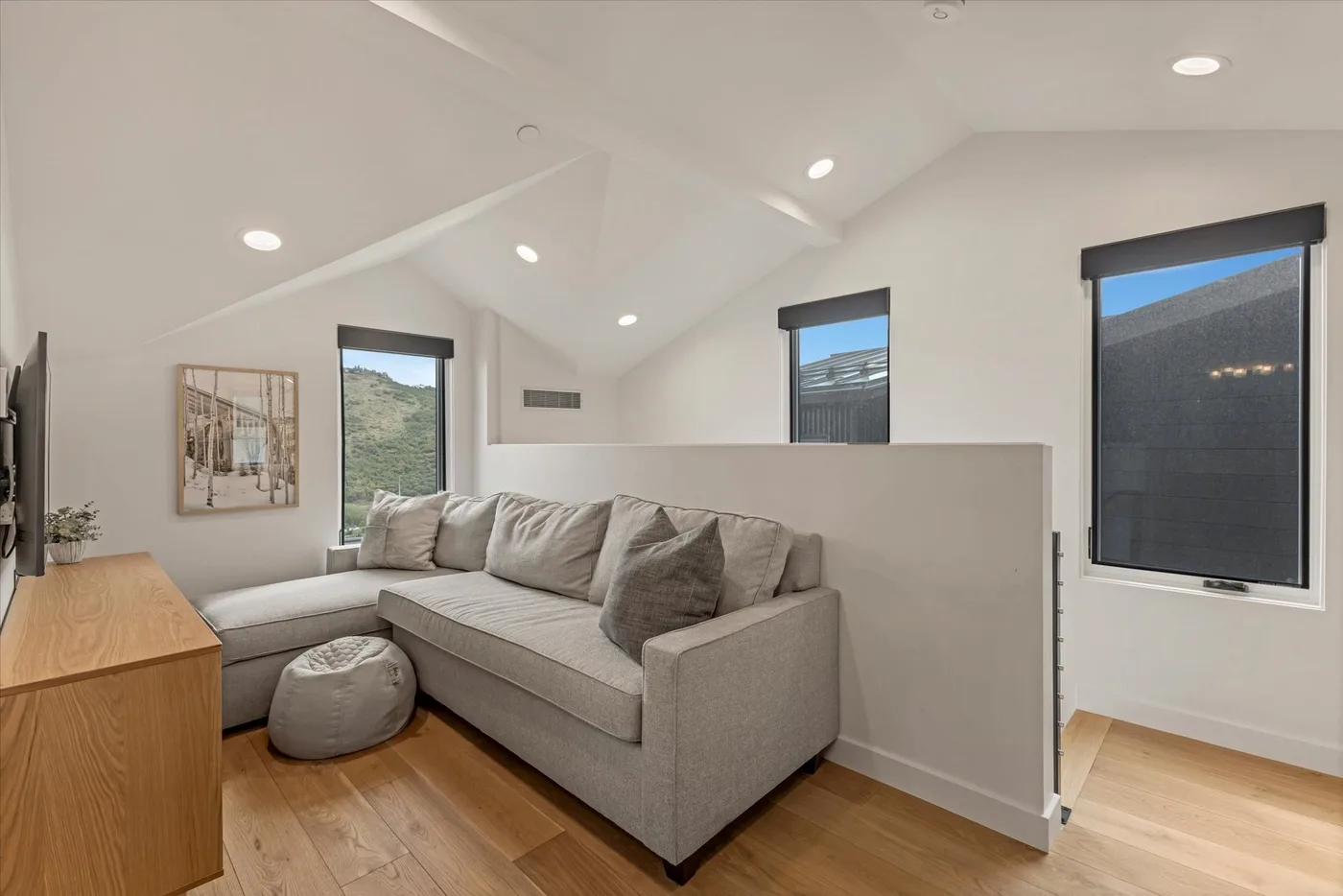 A bright living room with a sectional sofa, wood flooring, and large windows.